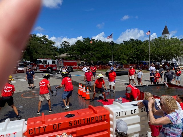 SJFD volunteers in red shirts running the Bucket Brigade relay in front of City of Southport barriers