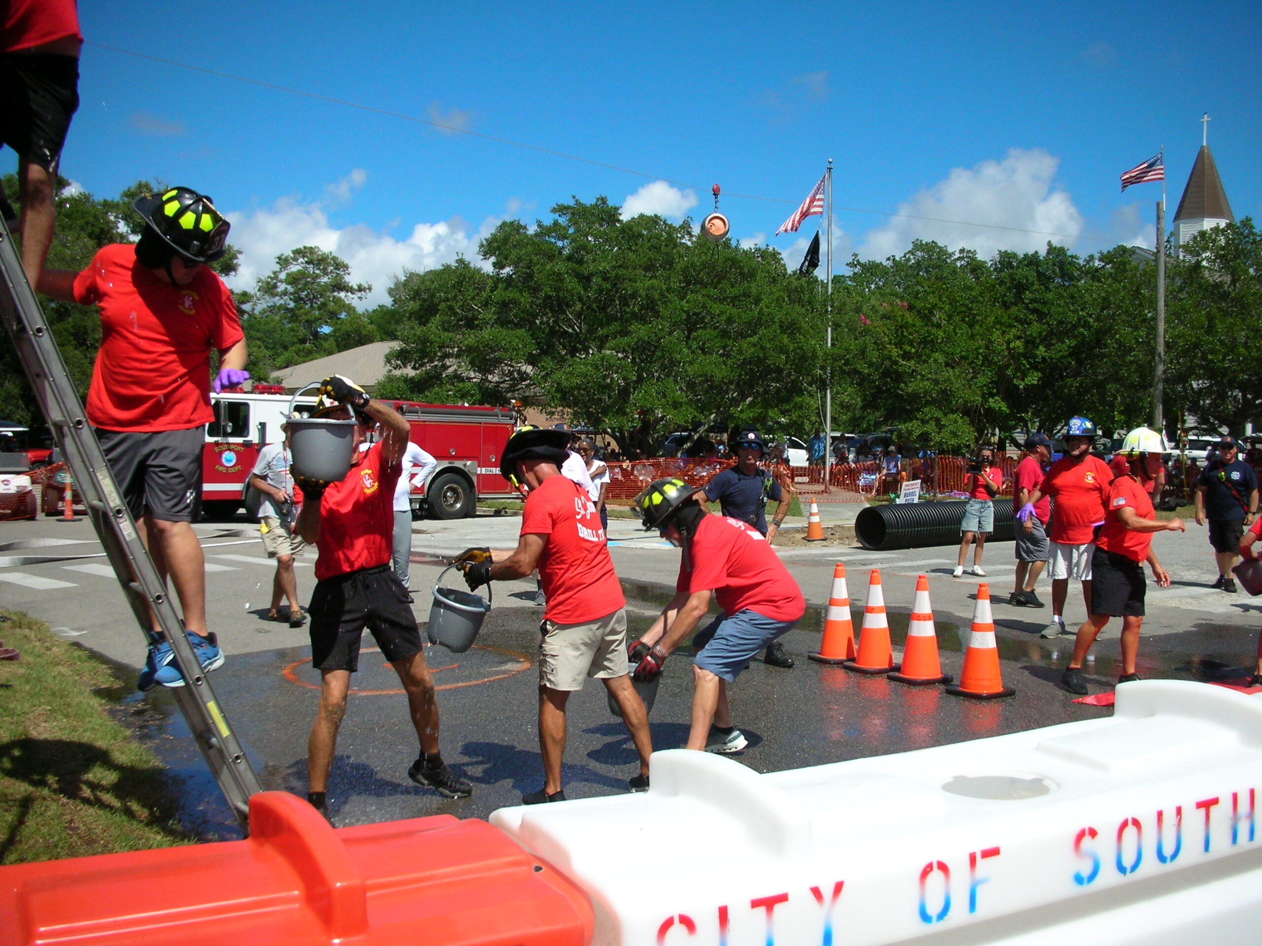 SJFD volunteers in red shirts and helmets carrying buckets up the scaffold ladder at the City of Southport competition