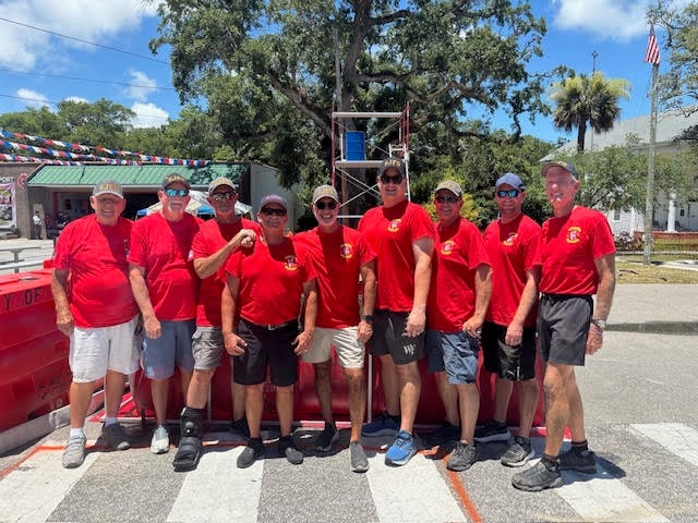 The St. James Fire Department competition team poses together in matching red SJFD shirts in front of the Bucket Brigade scaffold