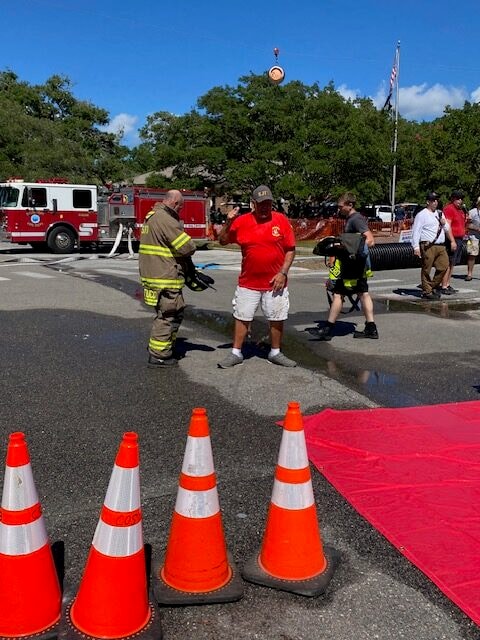 SJFD volunteer in red shirt confers with a firefighter between events on the wet competition course