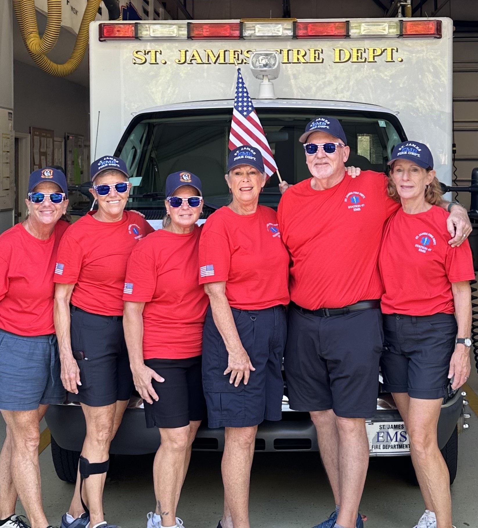 SJFD EMS volunteers in red shirts standing in front of the St. James Fire Dept. ambulance before the parade