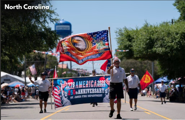 SJFD volunteers carrying the 1776–2026 America 250th Anniversary St. James Fire Department banner down the Southport parade route