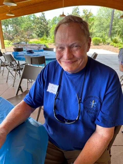 Bob Voss in his St. James EMS blue shirt smiles at the camera at the picnic pavilion