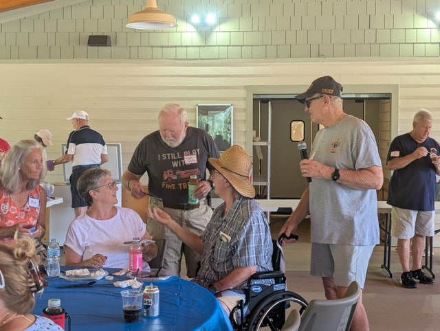 SJFD Chief with microphone chats with volunteers and families seated at tables inside the pavilion