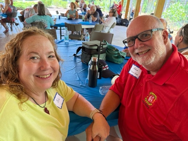 SJFD volunteer in red polo and guest in yellow shirt smile together at a picnic table