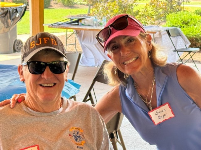 SJFD volunteer in an SJFD hat and Susan Boyer in a pink cap smile together at the picnic