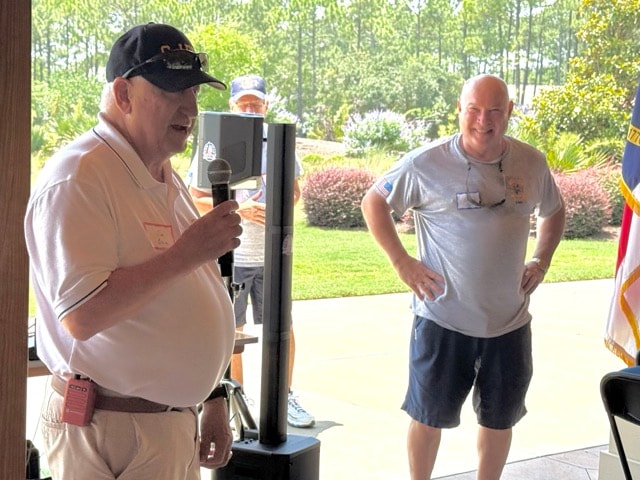 Two SJFD members at the microphone during the picnic program with the American flag in the background