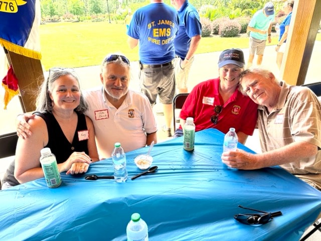 Four SJFD volunteers including an EMS member in a blue St. James shirt gather at a table