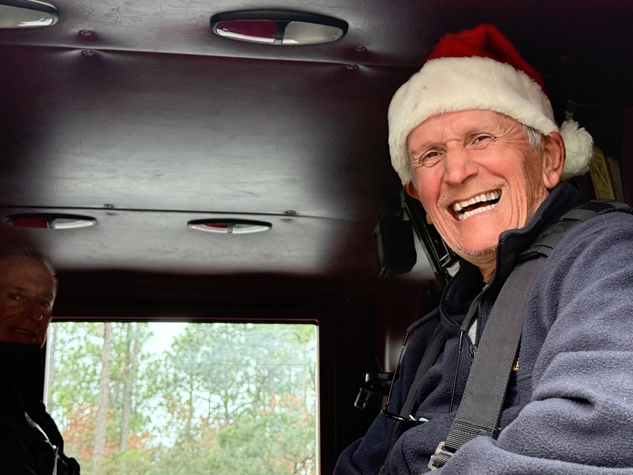 SJFD volunteer Harry Beutler grinning in a Santa hat from inside the cab of the fire truck