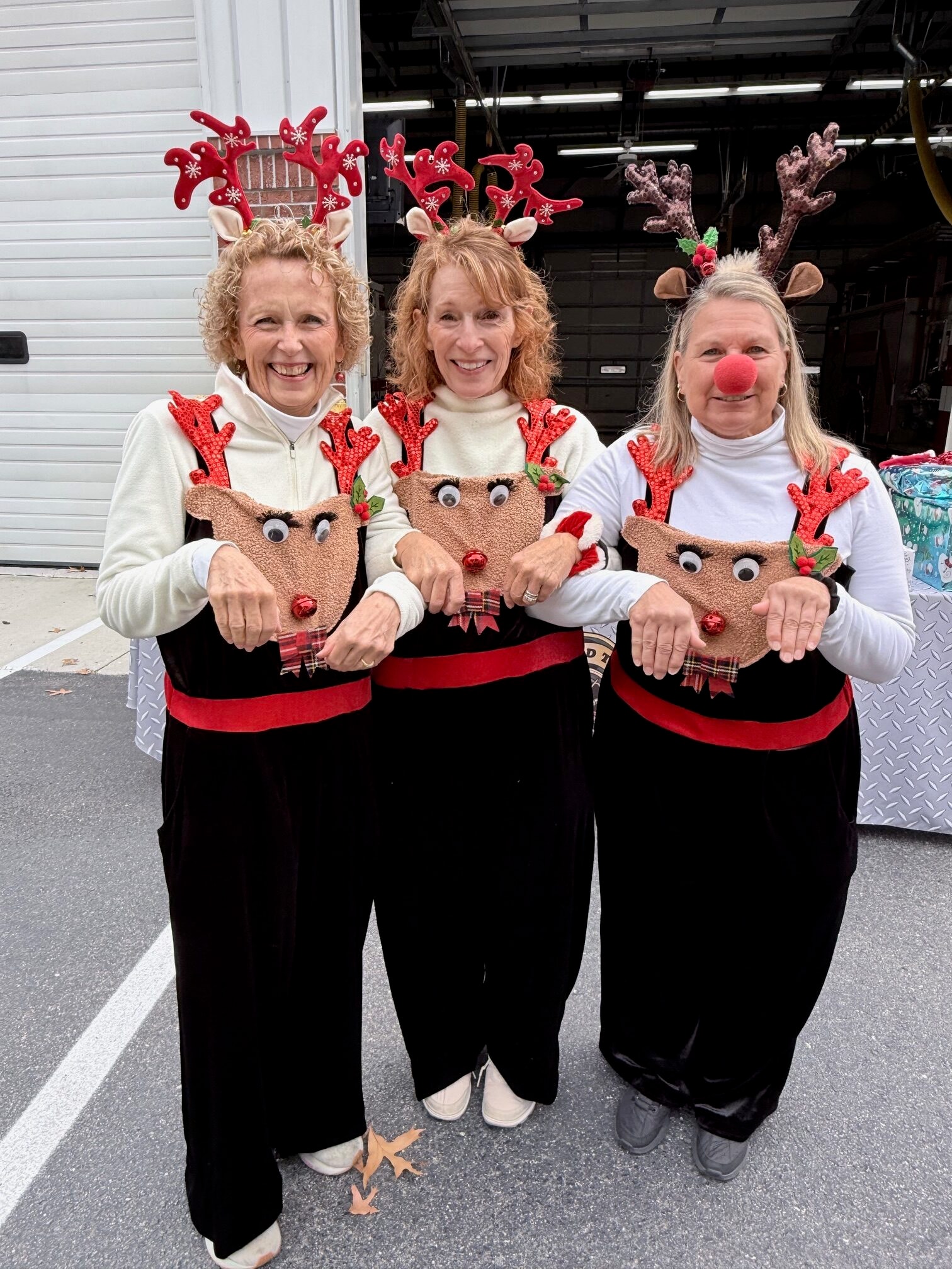 Three SJFD volunteers dressed as reindeer holding handmade reindeer crafts outside the station