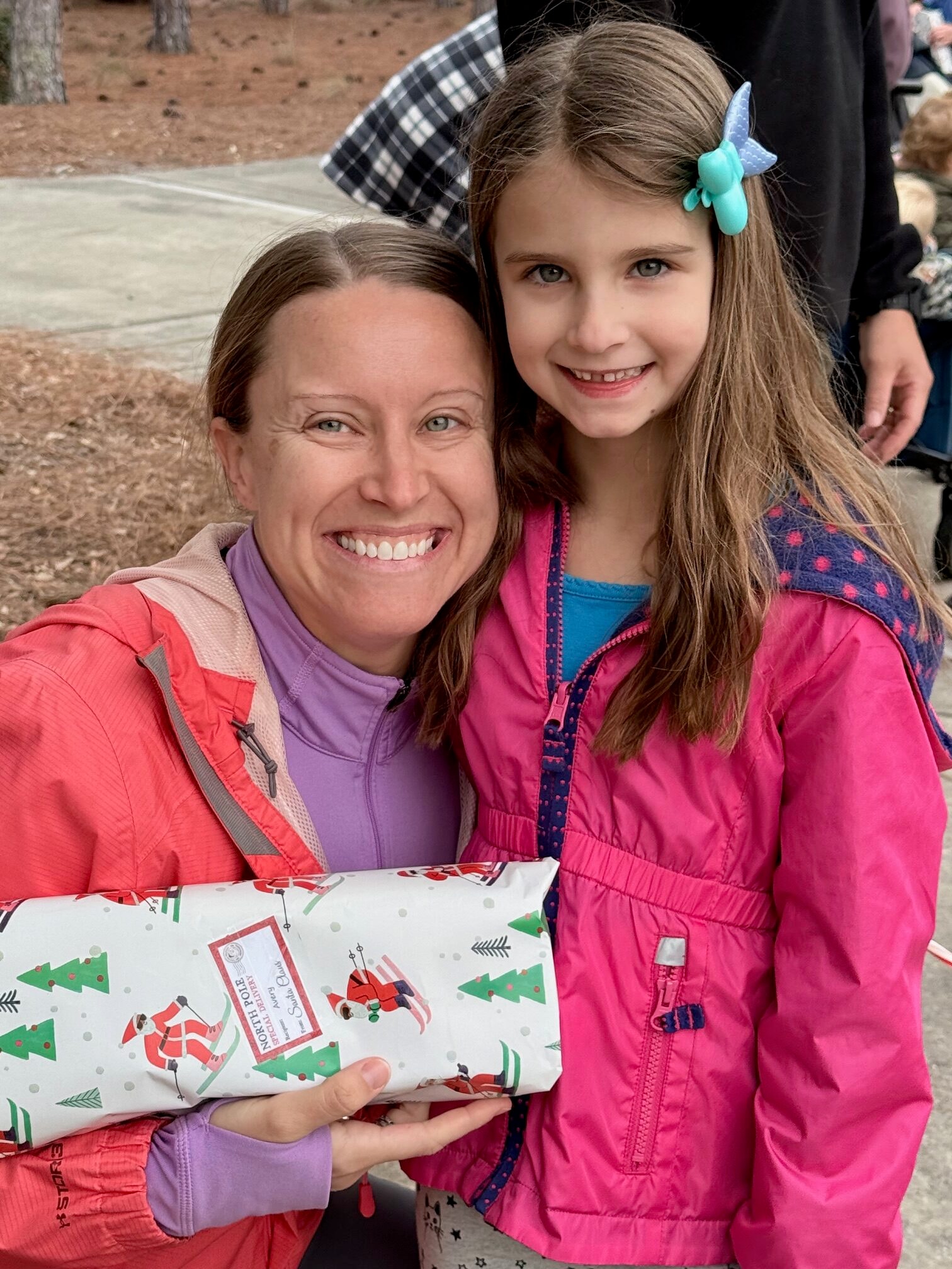 Mother and daughter smiling together holding a wrapped gift from Santa at the SJFD event